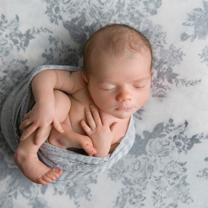 Sleeping newborn baby wrapped in soft grey fabric during studio session
