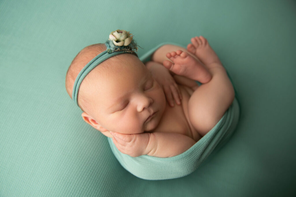 Sleeping newborn baby wrapped in teal fabric during a newborn photography session