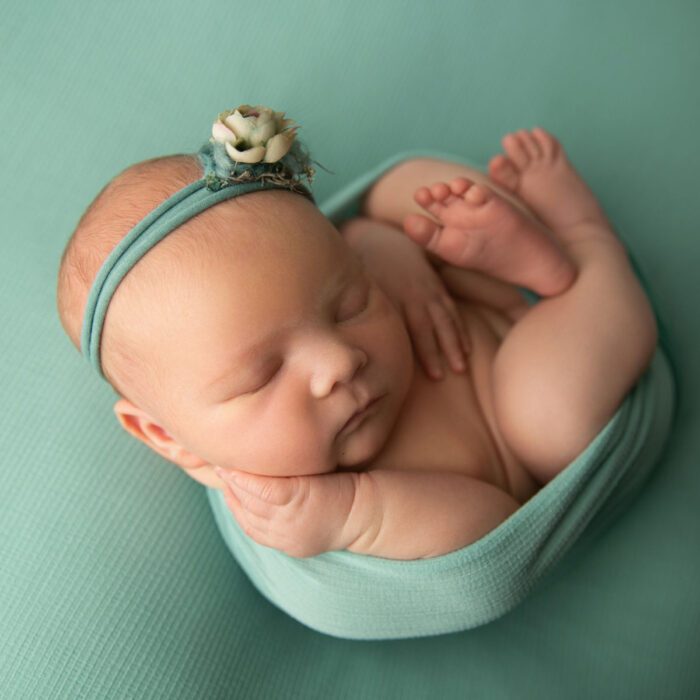 Sleeping newborn baby wrapped in teal fabric during a newborn photography session