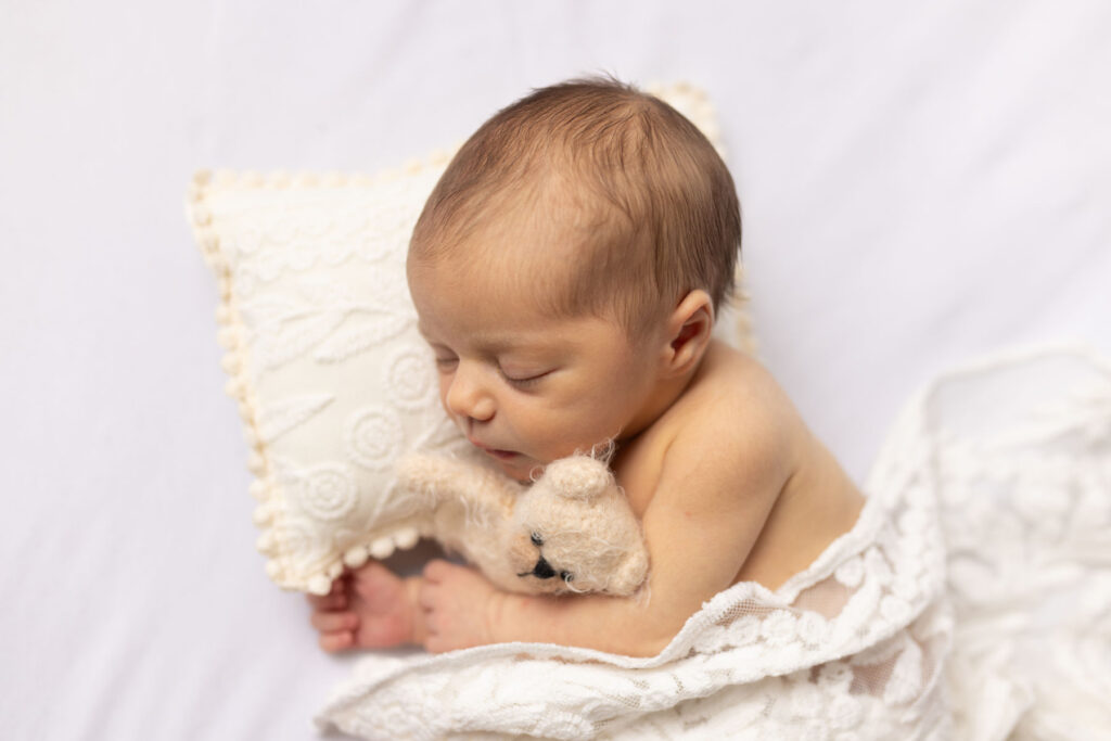 Sleeping newborn baby resting beside teddy bear during studio portrait session
