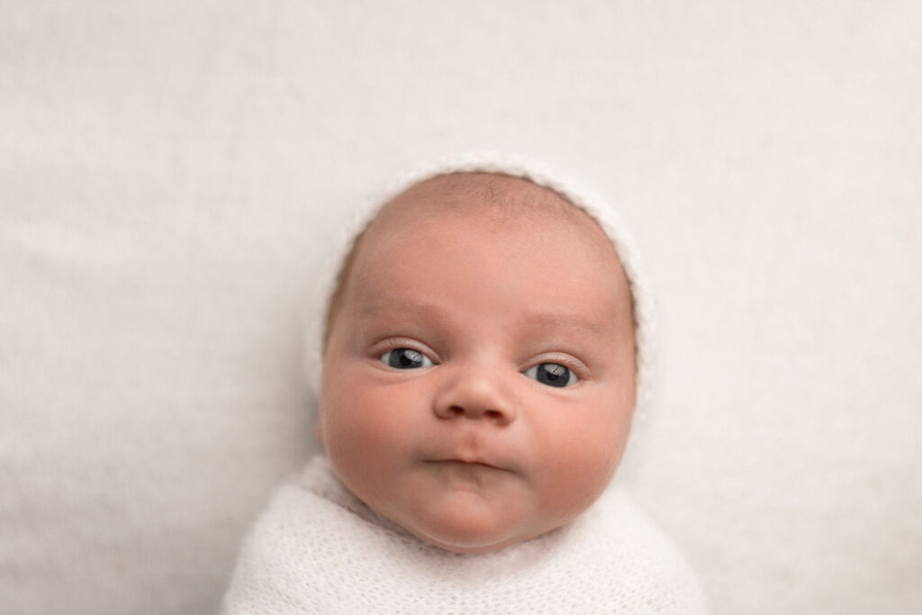 Close-up portrait of a newborn baby wrapped in cream fabric with soft neutral tones