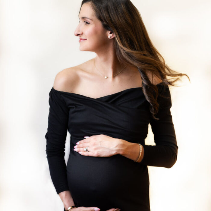 Pregnant mother in a black dress gently holding her baby bump during a studio maternity portrait