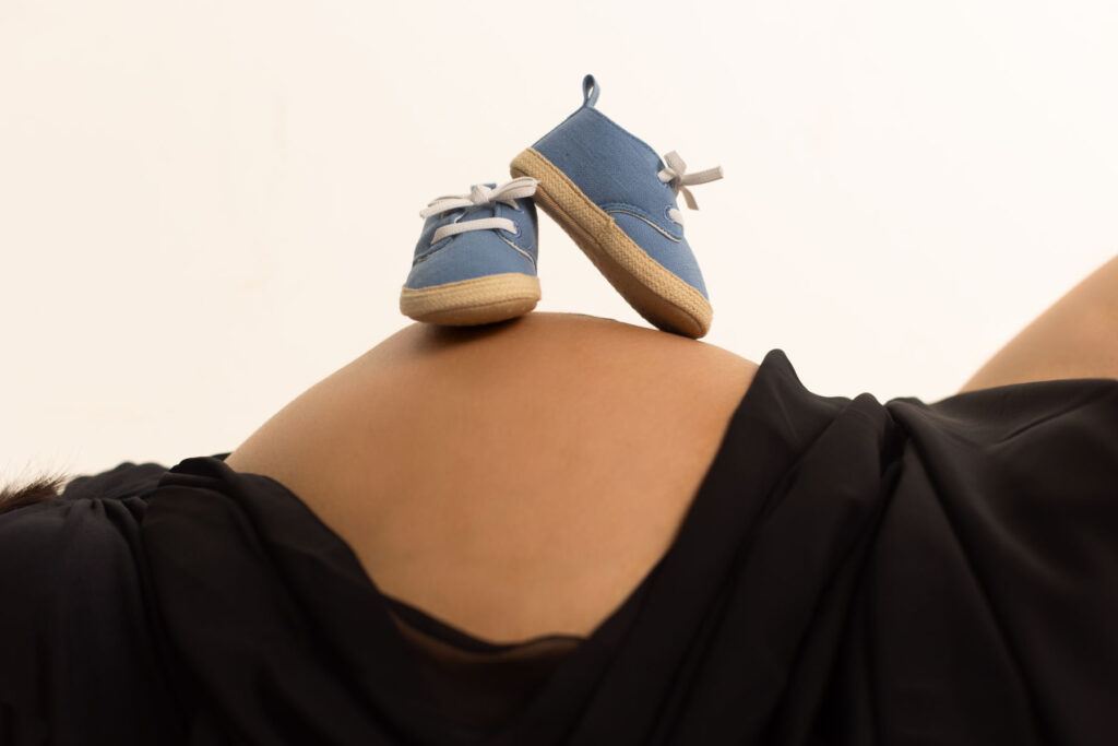 Blue baby shoes resting on a pregnant mother's belly during a maternity session