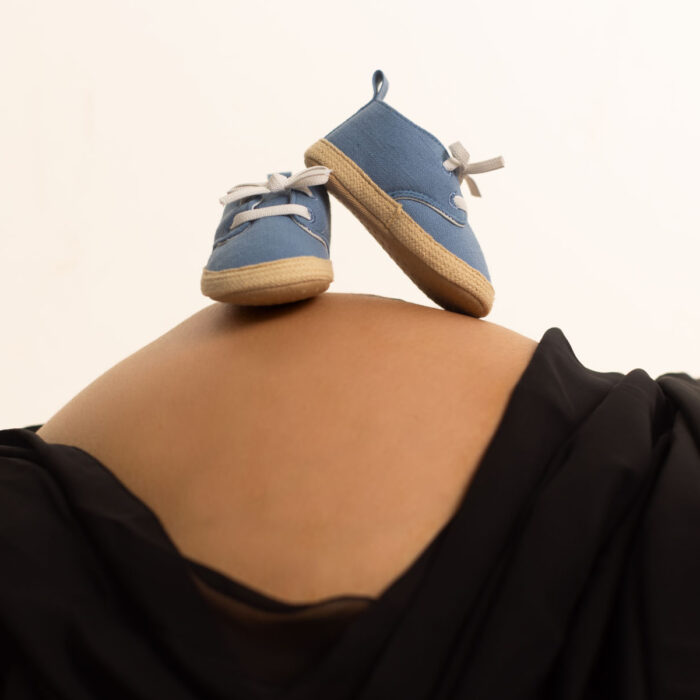 Blue baby shoes resting on a pregnant mother's belly during a maternity session