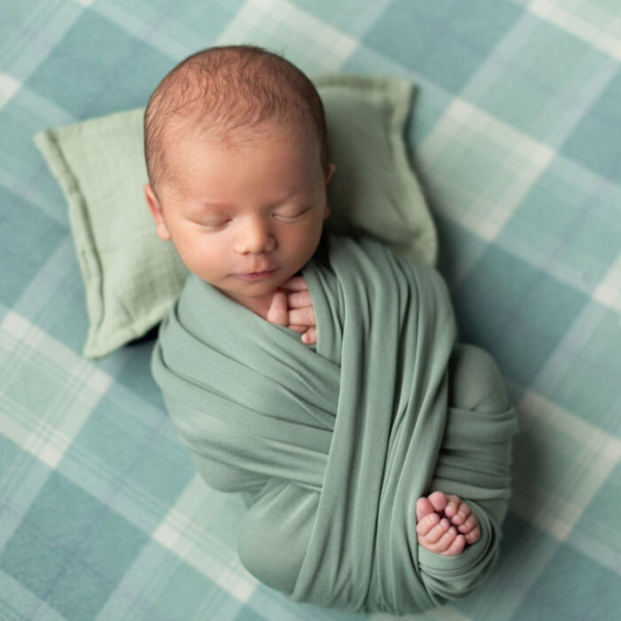 Sleeping newborn baby wrapped in green fabric on a soft textured background