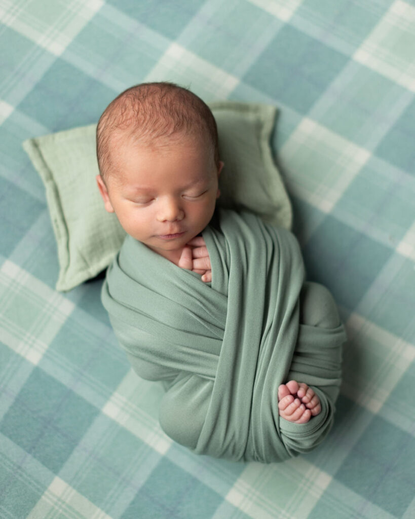 Sleeping newborn baby wrapped in green fabric on a soft textured background