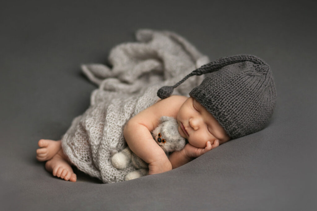 Sleeping newborn baby wearing gray knit hat and wrapped in soft textures