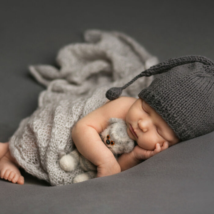 Sleeping newborn baby wearing gray knit hat and wrapped in soft textures