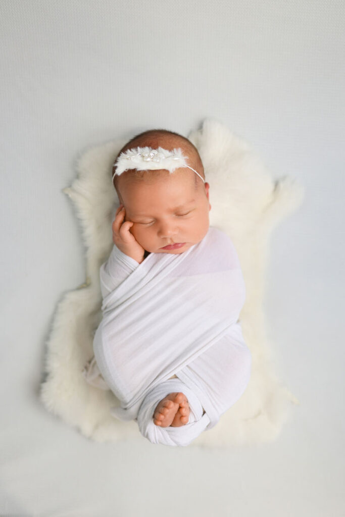 Sleeping newborn baby wrapped in white with delicate headband during studio session