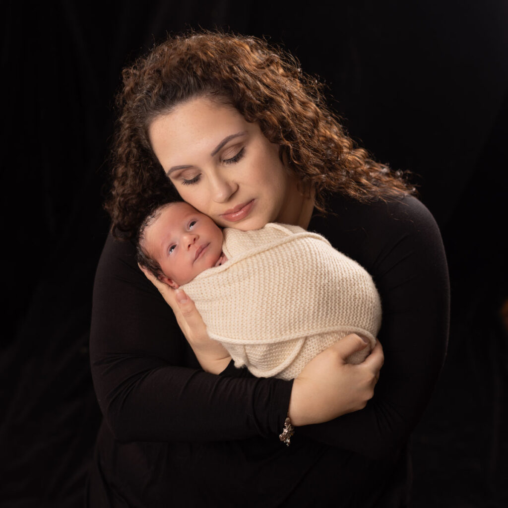 Mother holding her newborn baby wrapped in a soft blanket during a studio photography session