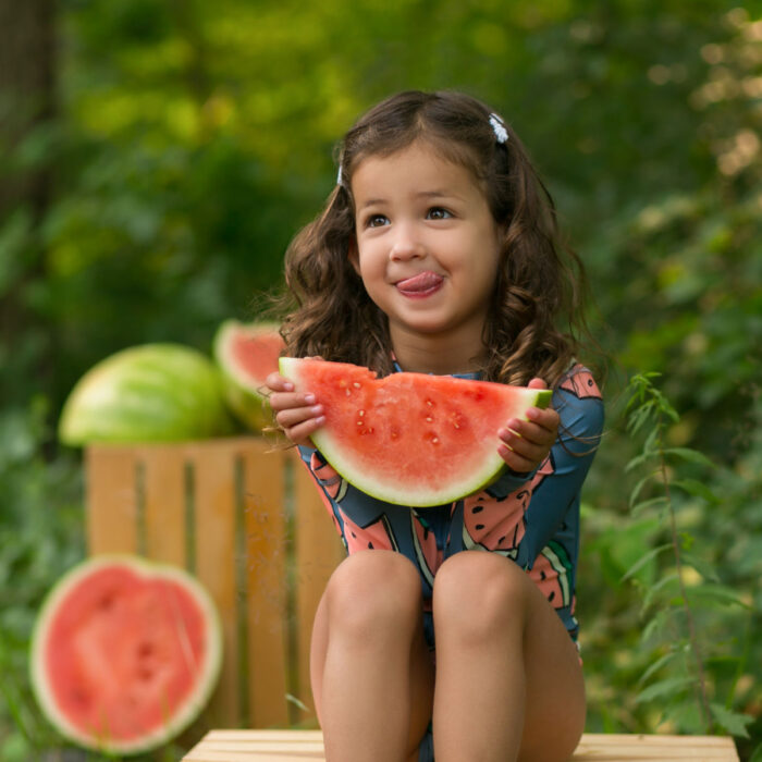 Young girl enjoying watermelon during an outdoor summer children's photography session.