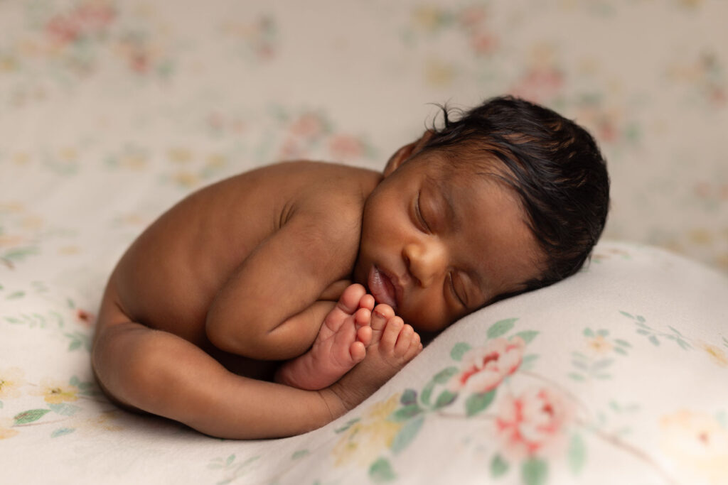 Sleeping newborn baby posed naturally on a floral pillow during a newborn photography session