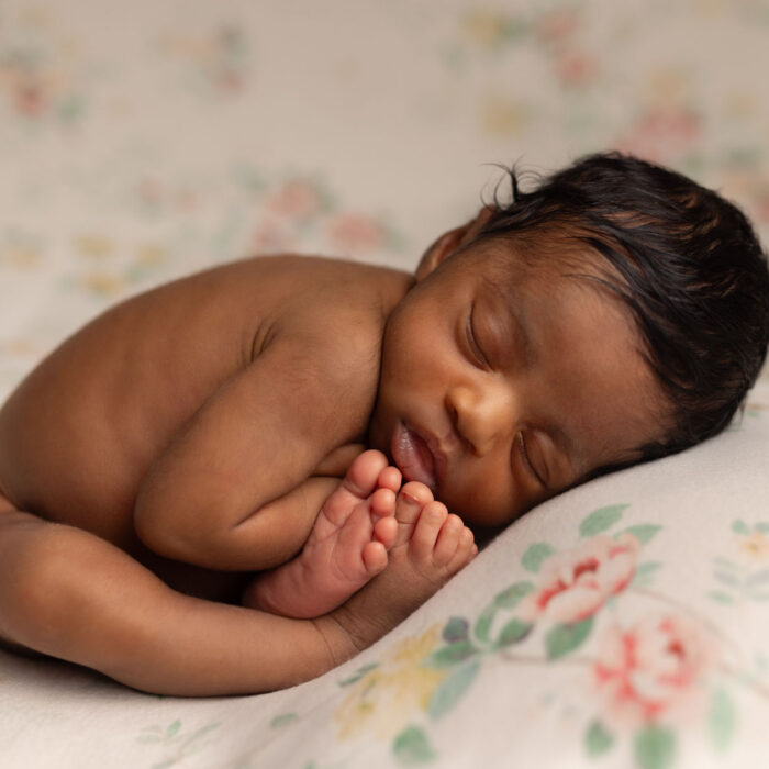 Sleeping newborn baby posed naturally on a floral pillow during a newborn photography session