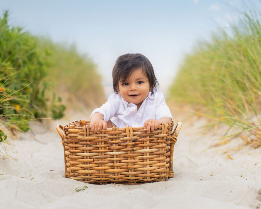 Young child sitting in a basket during a beach portrait session surrounded by sand dunes