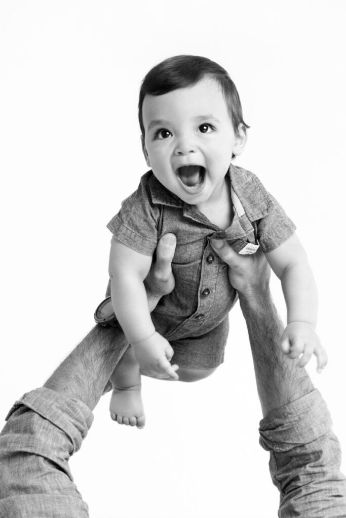 Black and white portrait of smiling baby lifted into the air during a studio session