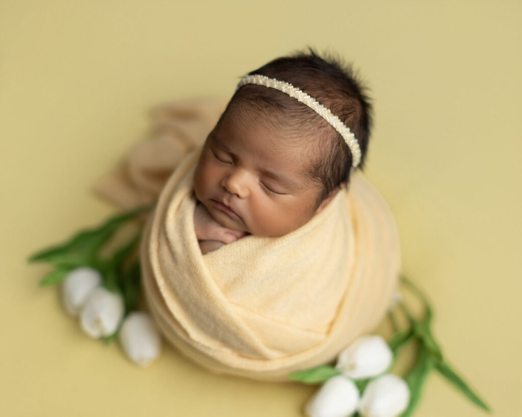 Sleeping newborn wrapped in soft fabric surrounded by white tulips during a studio session