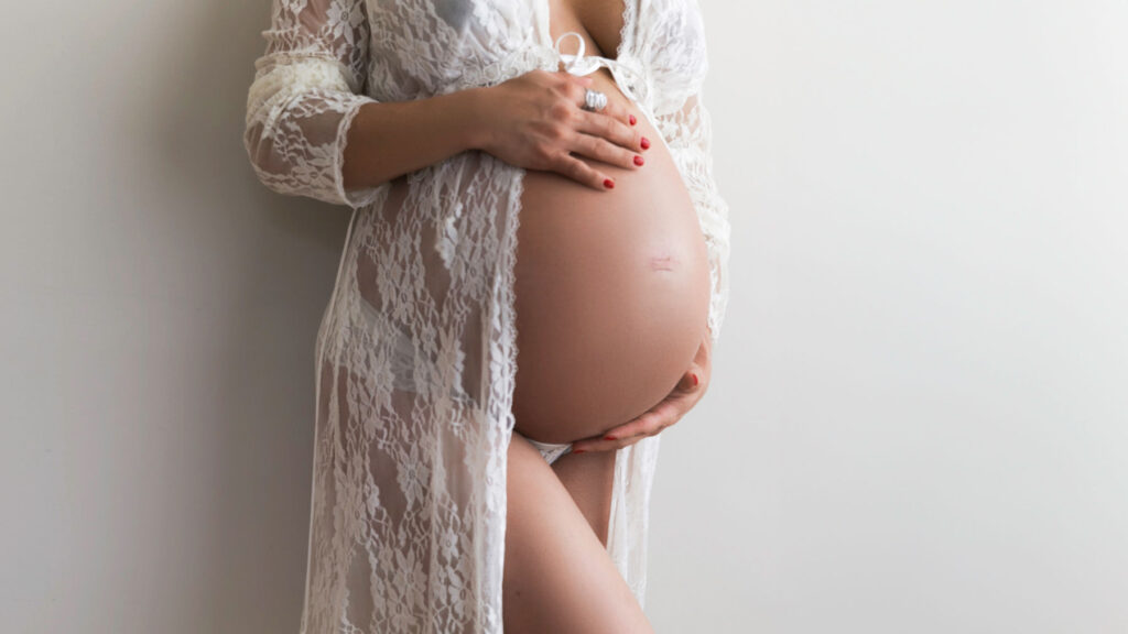 Elegant maternity portrait featuring expectant mother wearing white lace during a studio session