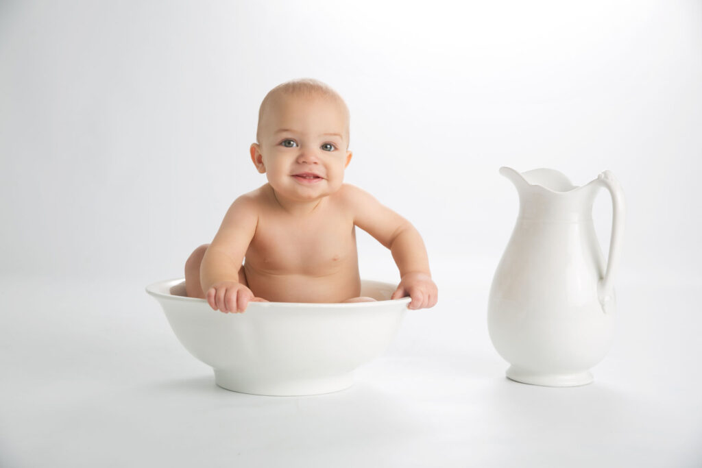 Smiling baby sitting in a white bowl during a milestone portrait session