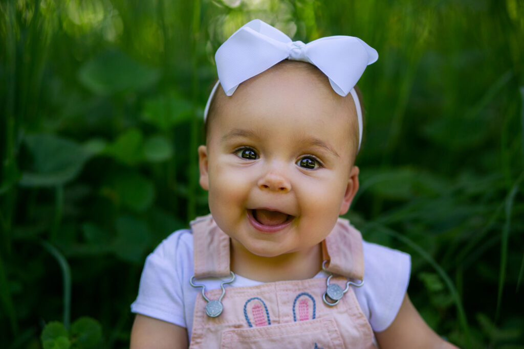 Smiling baby girl wearing a white bow during an outdoor portrait session