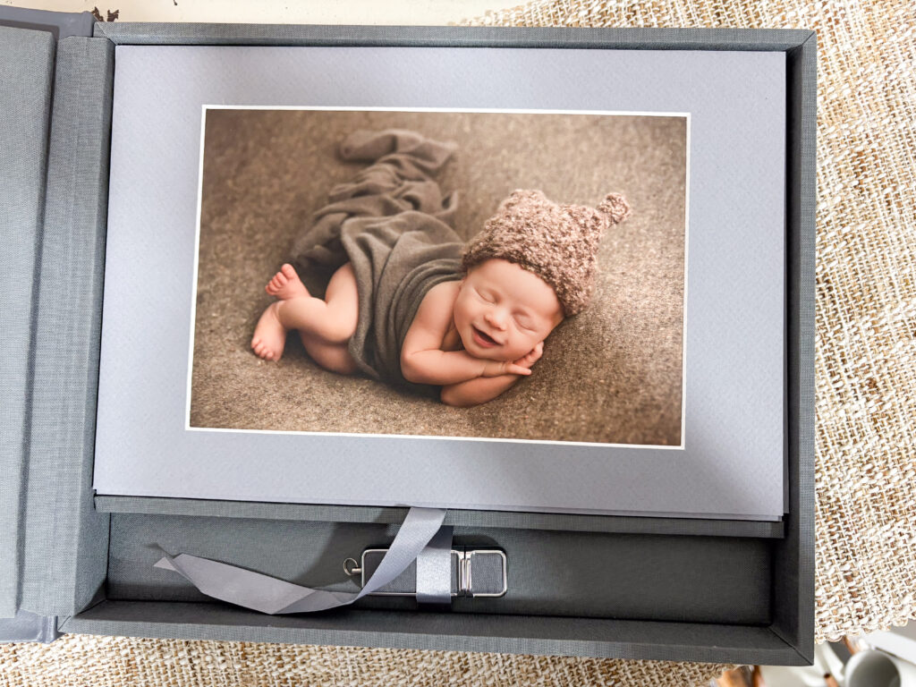 Matted newborn portrait displayed in a leather keepsake box with a matching USB drive from Alternate Angles Photography
