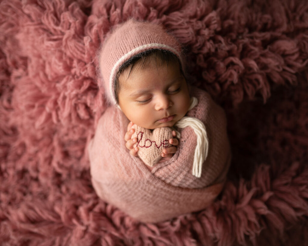 Sleeping newborn wrapped in soft pink holding a heart during a studio newborn photography session