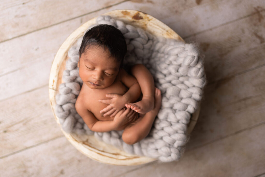 Sleeping newborn resting in a bowl with soft gray knit textures during a studio portrait session