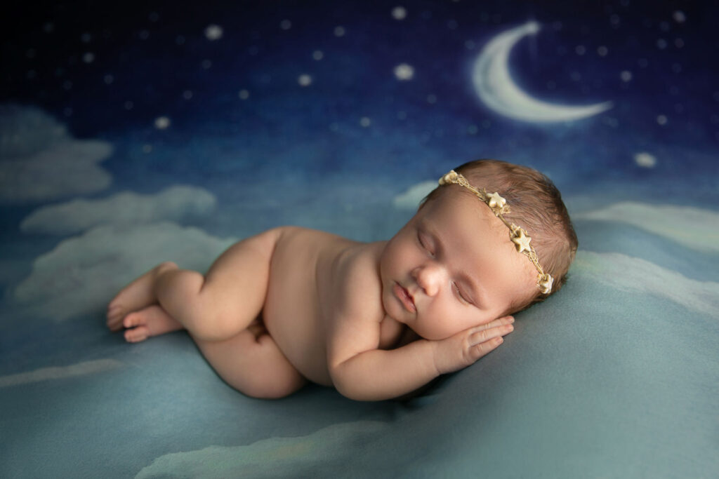 Sleeping newborn posed on a moon and stars themed backdrop during a studio session