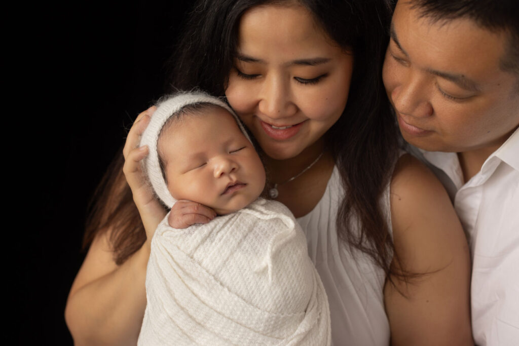 Mother and father holding their sleeping newborn baby boy in a professional studio family portrait