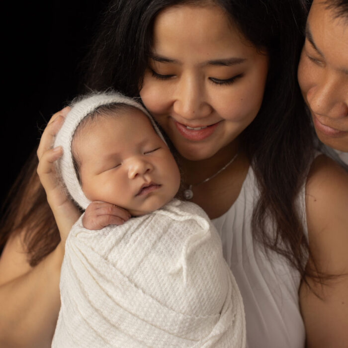 Mother and father holding their sleeping newborn baby boy in a professional studio family portrait