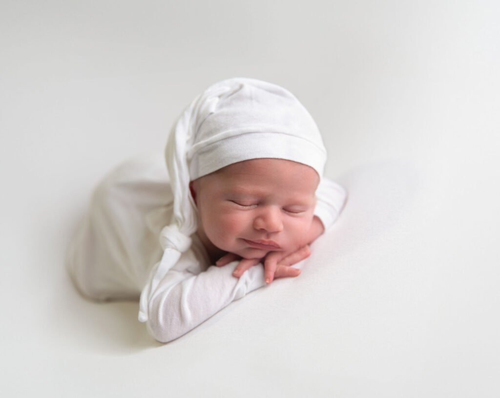 Sleeping newborn baby wearing a white hat and outfit during a minimalist studio newborn session