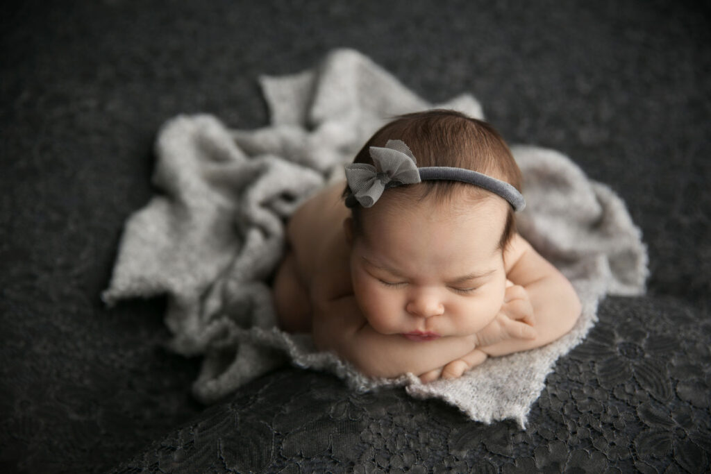 Sleeping newborn baby girl wearing a grey bow headband during a posed studio newborn photography session