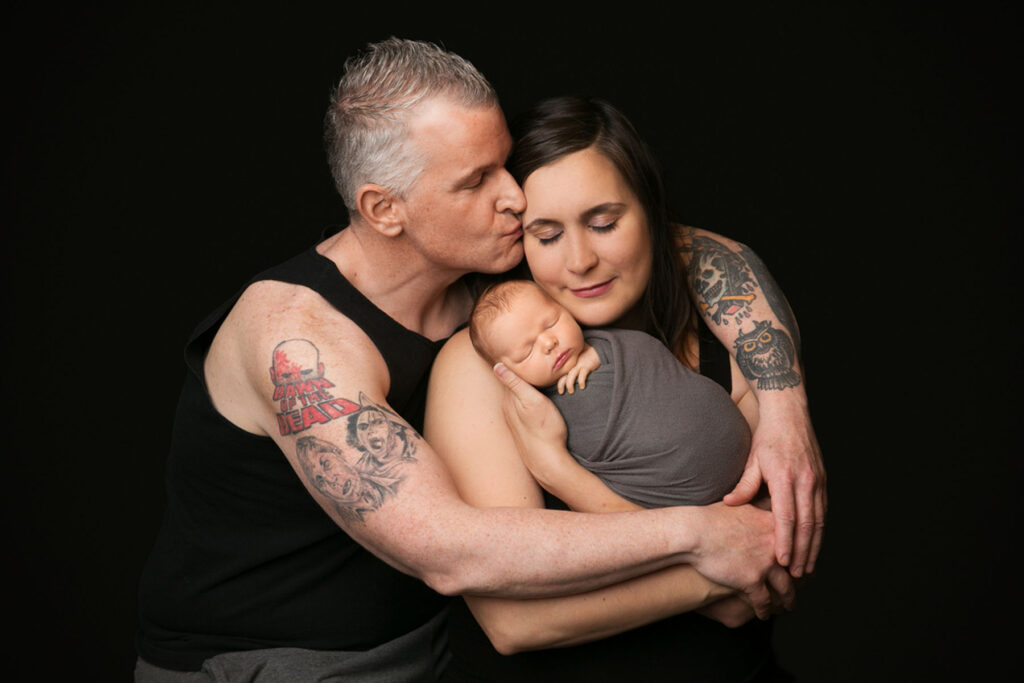 Parents embracing their sleeping newborn baby during an emotional studio family portrait session