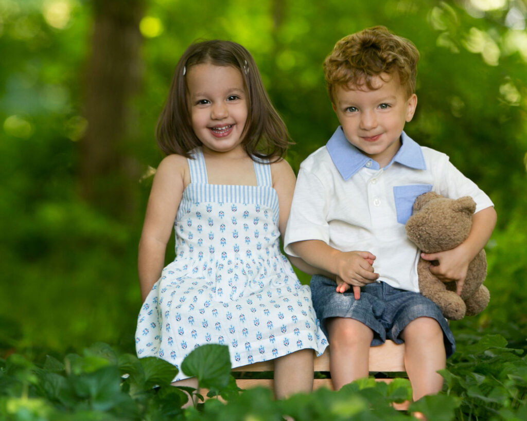 Smiling young brother and sister sitting together outdoors during a professional sibling portrait session