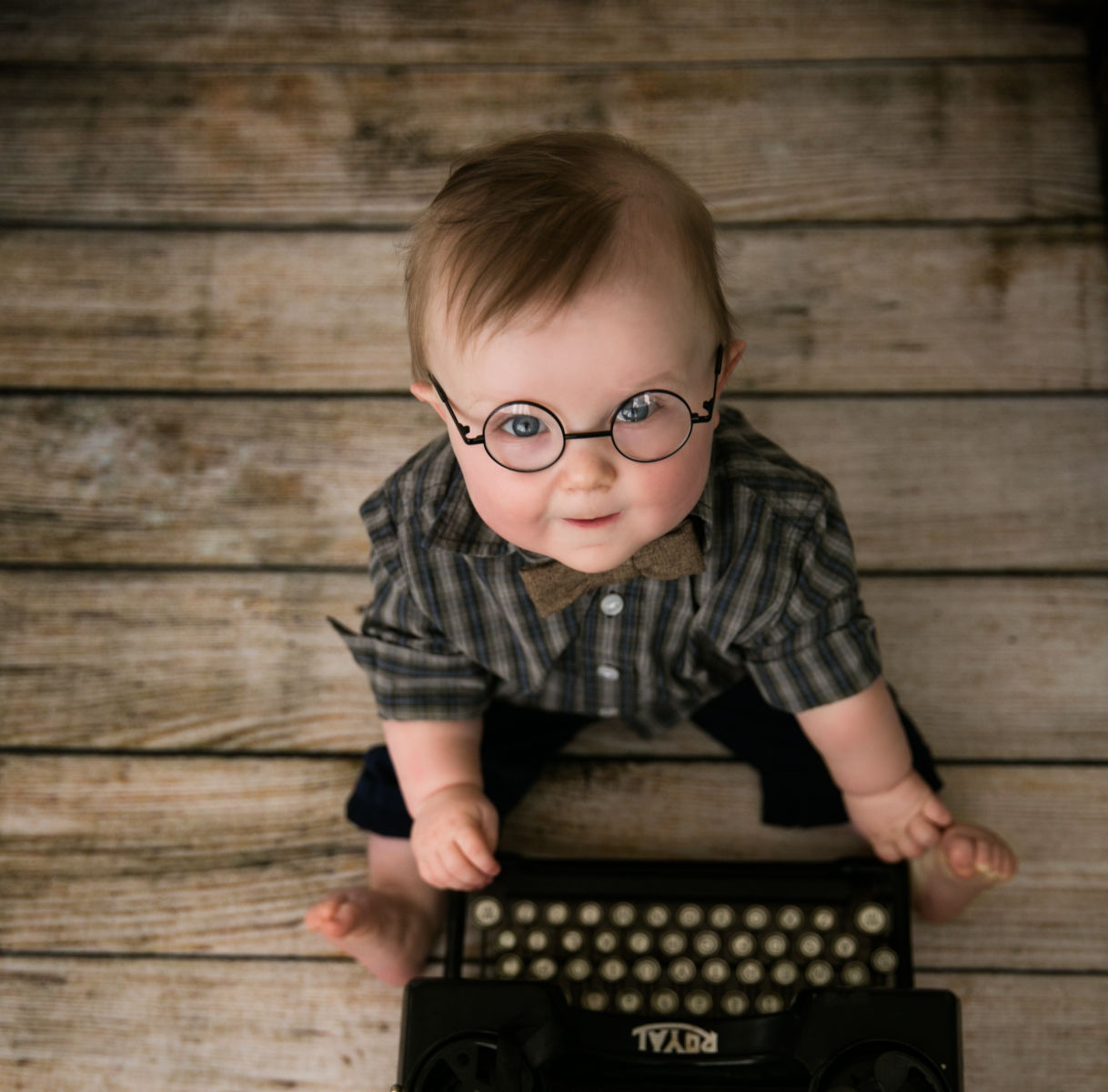 Baby boy wearing glasses sitting beside vintage typewriter during milestone sitter photography session