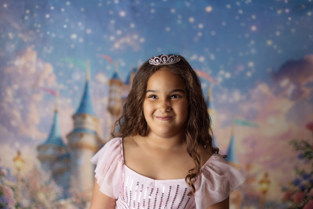 Smiling 6 year old girl wearing a pink dress and tiara during a princess themed child portrait session at Alternate Angles Photography studio