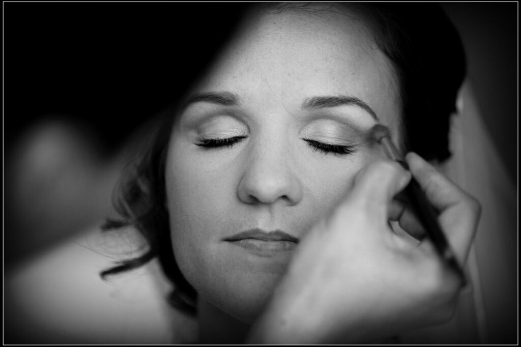 Bride having eye makeup applied during a black-and-white getting-ready moment before the wedding ceremony