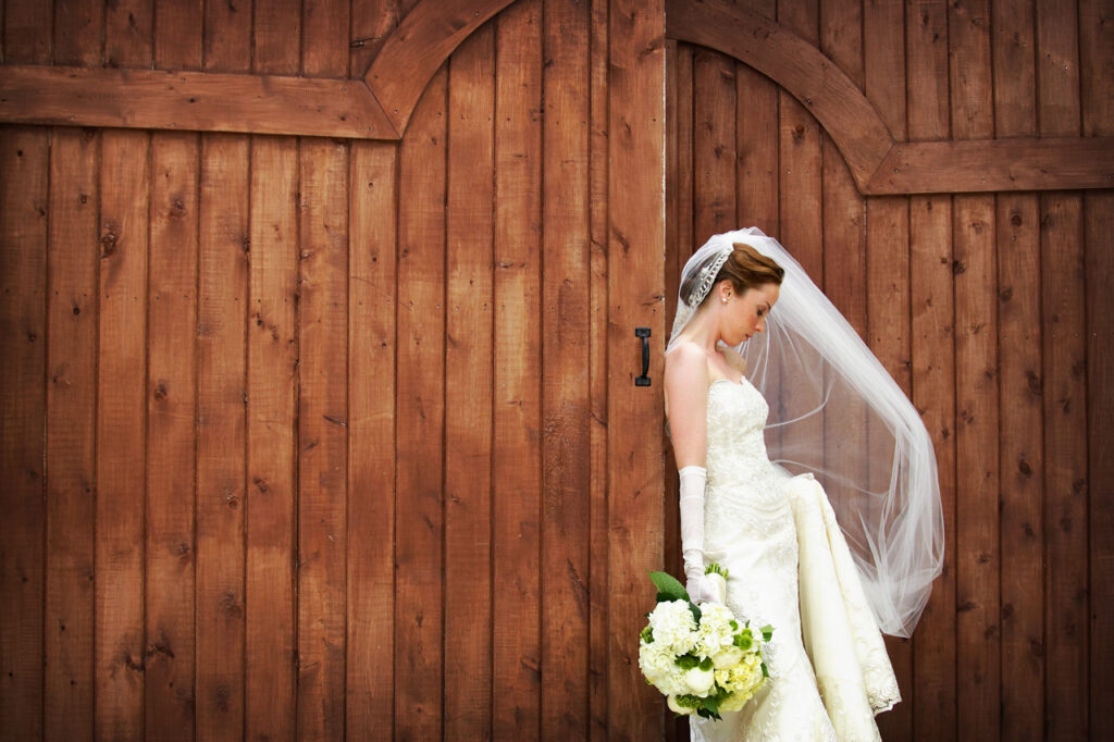 Bride holding her bouquet beside rustic wooden doors during a bridal portrait session at Belle Mer in Newport Rhode Island