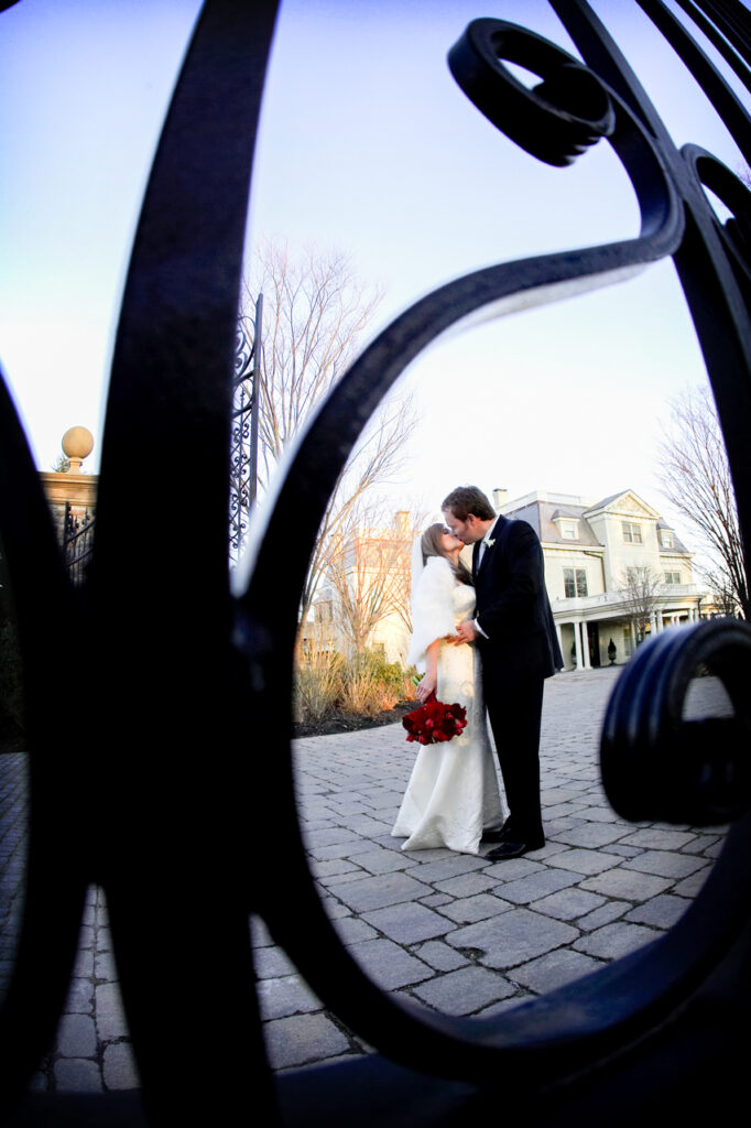 Bride and groom kissing during a wedding portrait framed through an iron gate at The Chanler in Newport Rhode Island