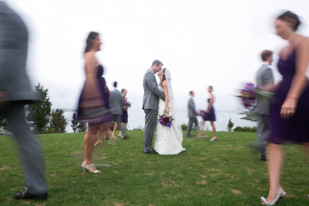Bride and groom kissing during a creative wedding party portrait as bridesmaids and groomsmen walk past in motion blur