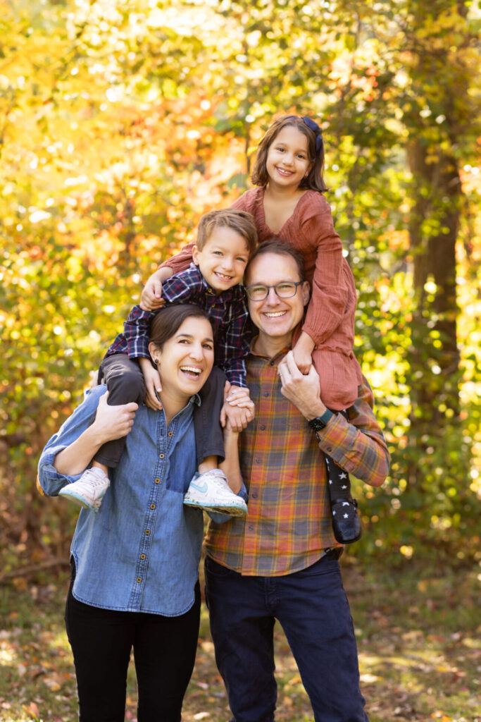 Family of four smiling together during an outdoor fall family photography session in Norwood, Massachusetts