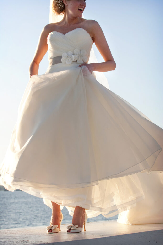 Bride standing on the wall at Belle Mer in Newport Rhode Island with her wedding dress flowing in the coastal light
