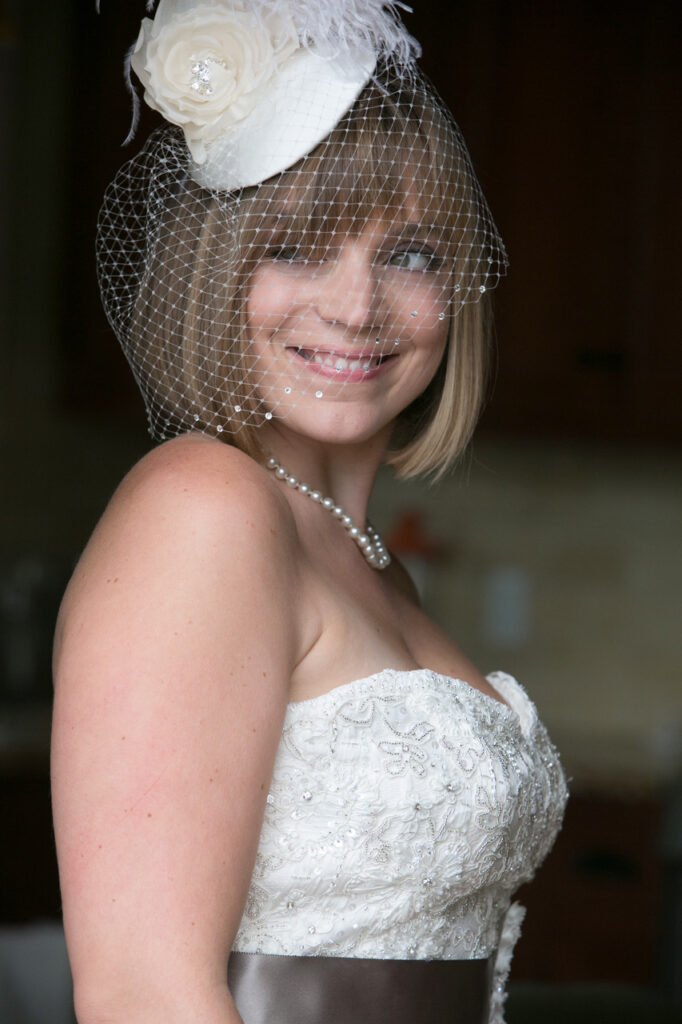Bride wearing a birdcage veil and floral headpiece smiling before walking down the aisle at her wedding ceremony