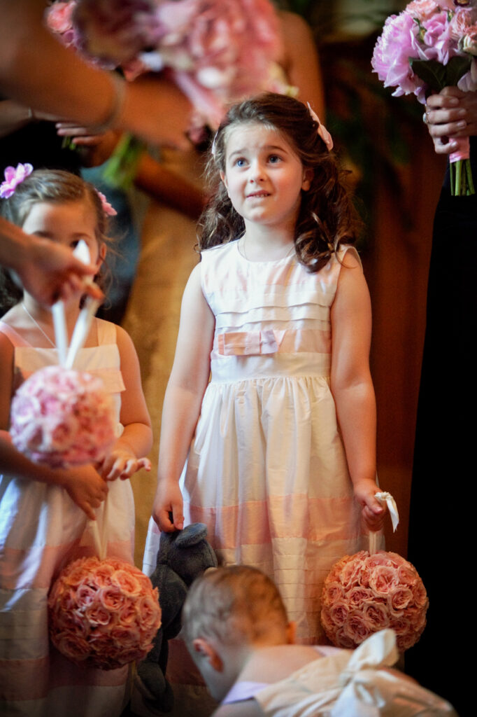 Flower girl holding a pink floral pomander while waiting with the bride and wedding party at the back of the church before walking down the aisle