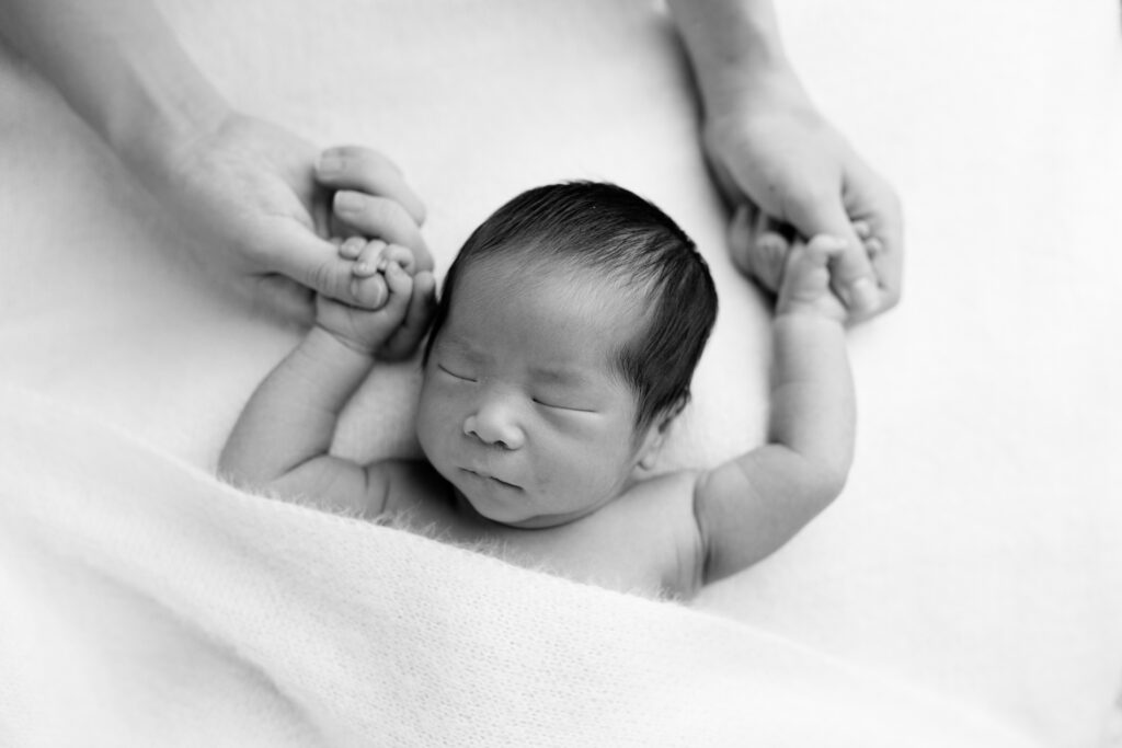 Japanese newborn baby holding parents hands in black-and-white close-up portrait