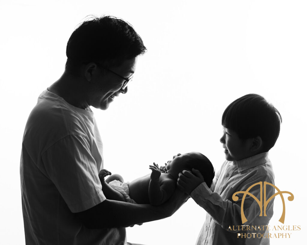 Proud Japanese father and big brother holding newborn baby in black-and-white portrait