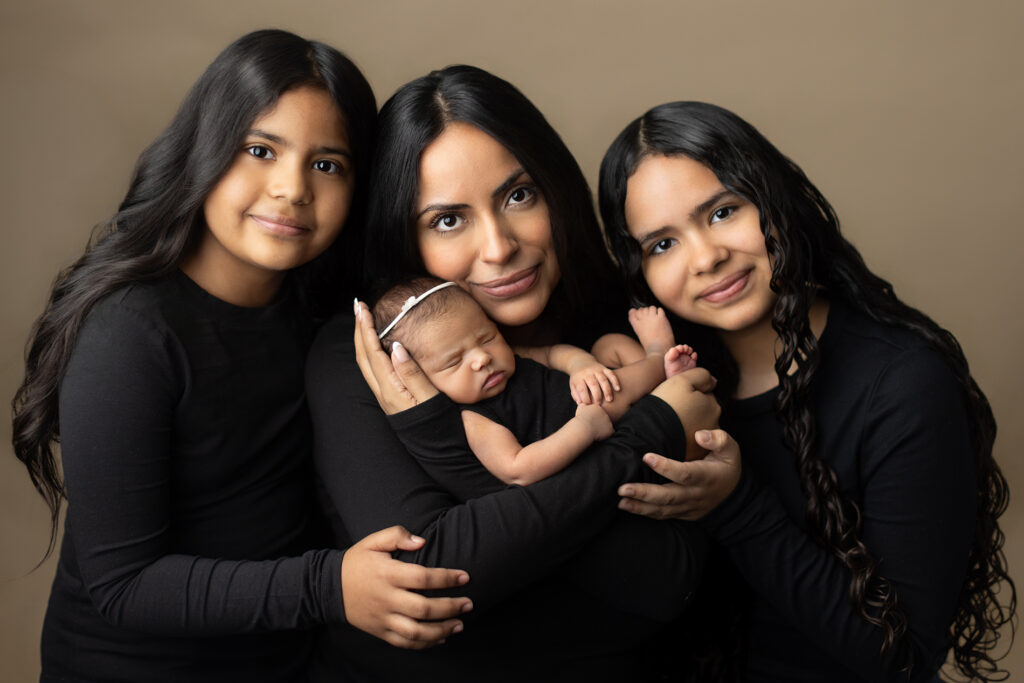 Mother holding newborn baby with her two older daughters during a studio family portrait session