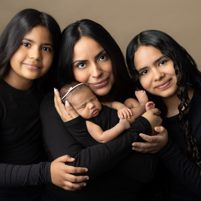 Mother holding newborn baby with her two older daughters during a studio family portrait session