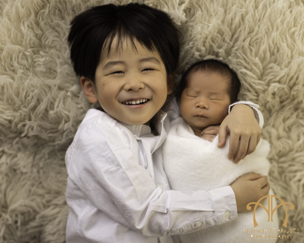 Proud Japanese big brother smiling while cuddling newborn baby in Boston studio