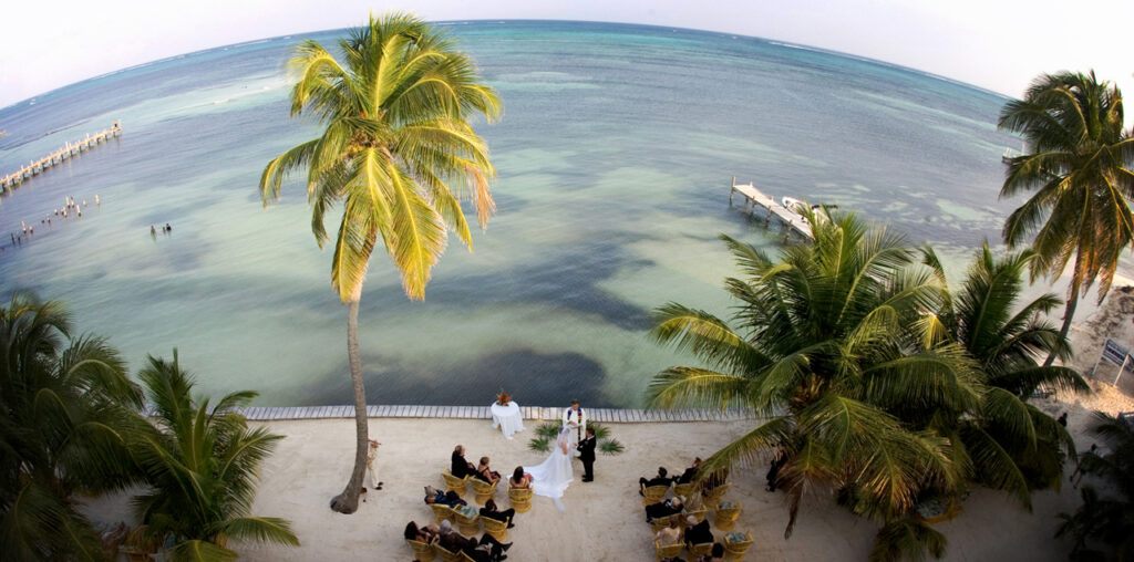 Belize destination wedding ceremony on the beach photographed from a hotel rooftop with palm trees and turquoise ocean water